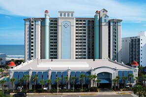 Un gran hotel con varios pisos, una destacada torre de reloj y vista al océano.