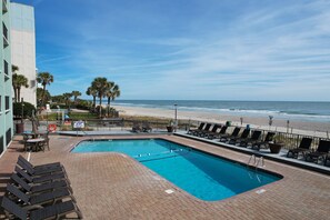 A swimming pool with lounge chairs and a view of the beach.