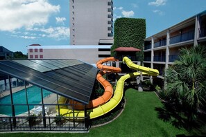 A rooftop pool area with a water slide, surrounded by a well-maintained lawn and a building with balconies.