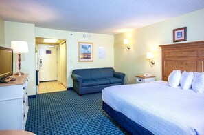 Habitación de hotel con cama, sofá, escritorio con lámpara, teléfono y un cuadro en la pared.