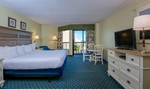 Habitación de hotel con una cama grande, televisor, escritorio con lámpara y balcón con vistas.
