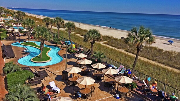 A resort with a swimming pool, beach, and outdoor seating area.