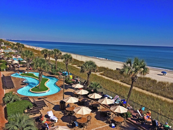 A resort with a swimming pool, beach, and outdoor seating area.