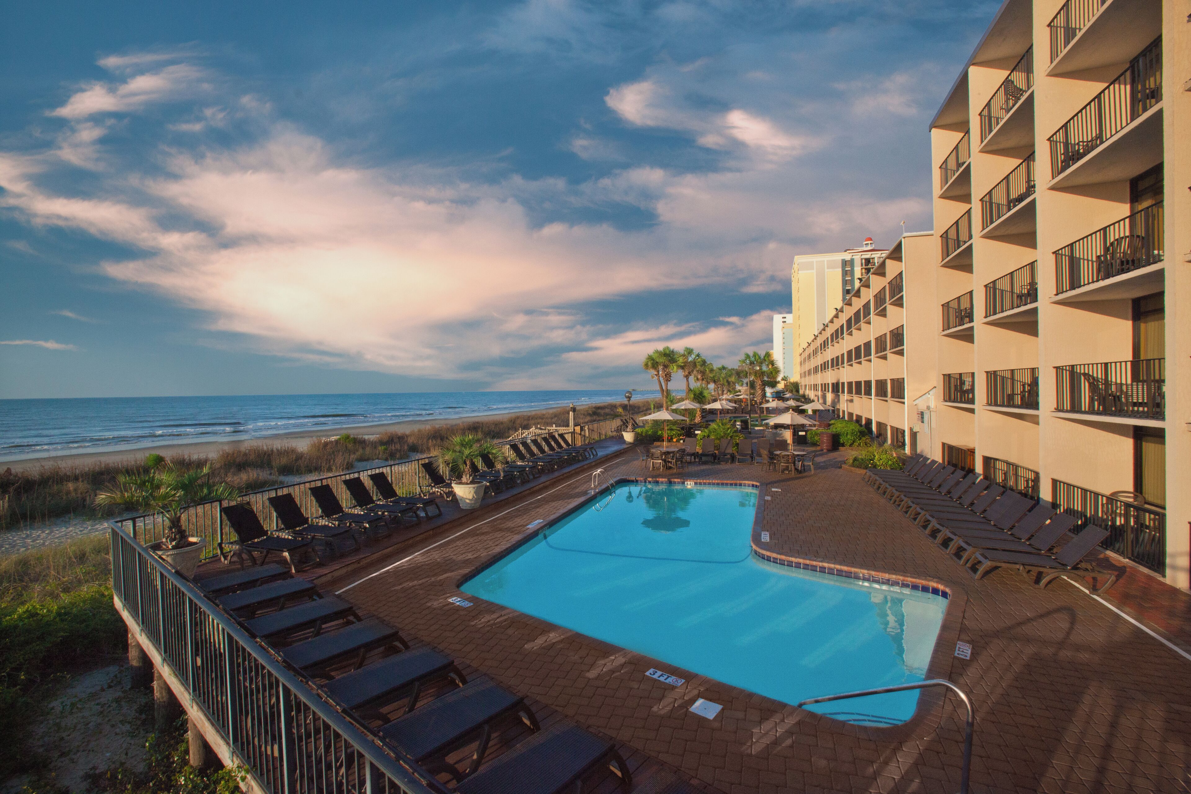 A hotel pool area with a view of the beach and ocean.