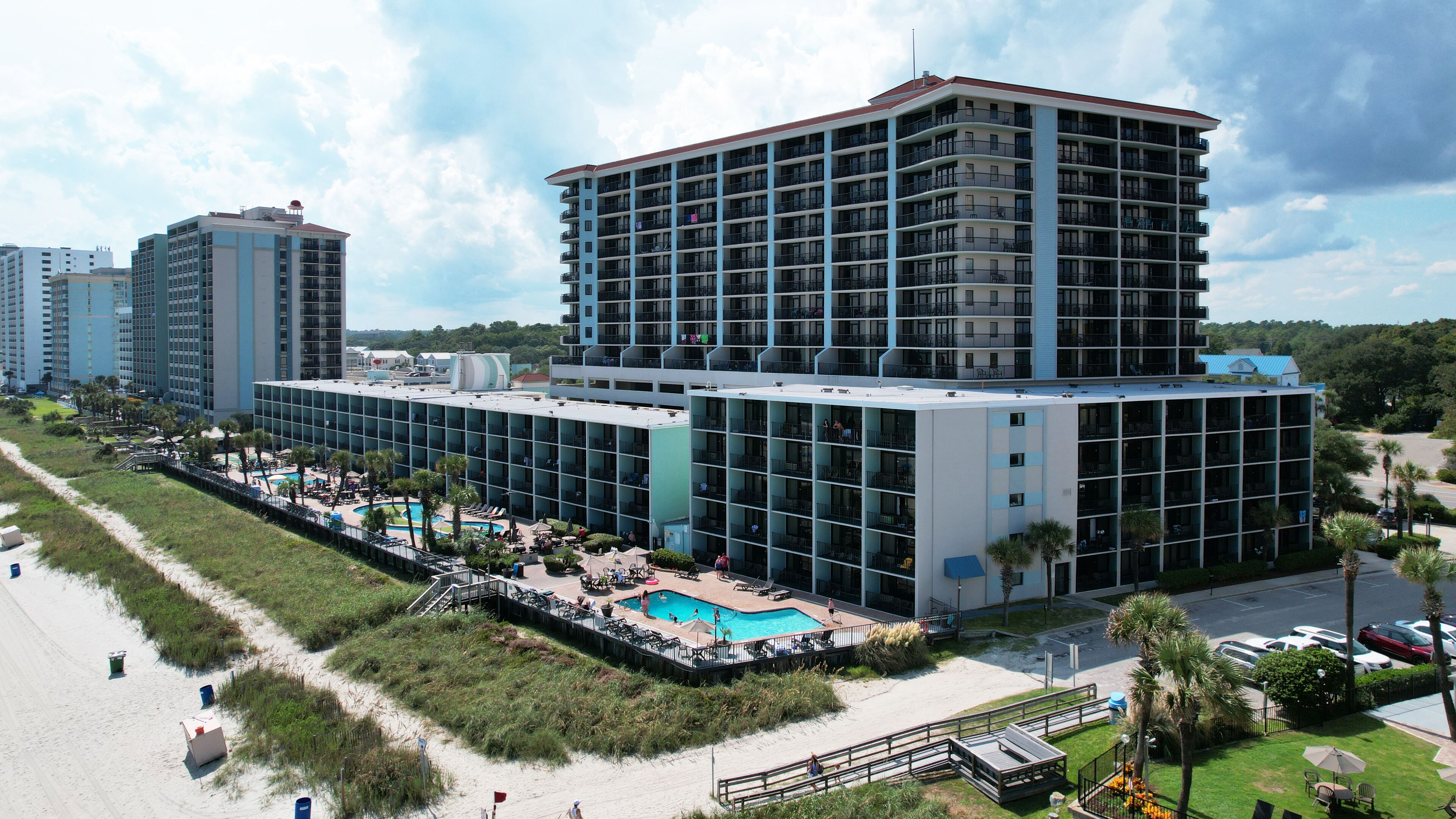 A multi-story hotel with a rooftop pool, surrounded by a beach and greenery.