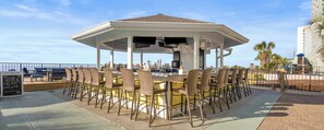 An outdoor bar area with a gazebo, multiple bar stools, and a view of the ocean.