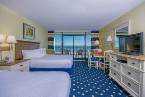 A hotel room with two beds, a television, a desk with a chair, and a view of the ocean.