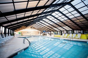 Una piscina interna con acqua cristallina, circondata da comode poltrone bianche e una zona coperta con struttura a tettoia in metallo.