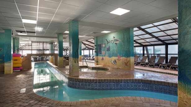 Une piscine intérieure avec des bords carrelés, des chaises longues et une fresque murale.