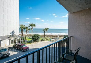 A balcony with a view of the beach, parked cars, and a building with a white facade. - Seaview Getaway 2 Queens, Ocean Balcony (Myrtle Beach)