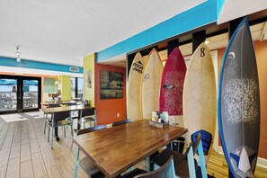 Interno di un ristorante con tavoli e sedie in legno e tavole da surf appese al muro.