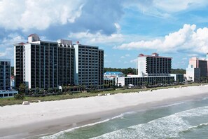 A beachfront hotel with multiple high-rise buildings, a sandy beach, and ocean waves. - Seaview Getaway 2 Queens, Ocean Balcony (Myrtle Beach)