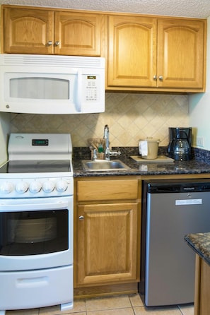 A compact kitchen with wooden cabinets, a white microwave, a stove, a sink, and a dishwasher. - Seaview Getaway 2 Queens, Ocean Balcony (Myrtle Beach)
