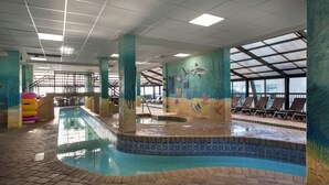 An indoor swimming pool with a tiled edge, lounge chairs, and a mural on the wall.