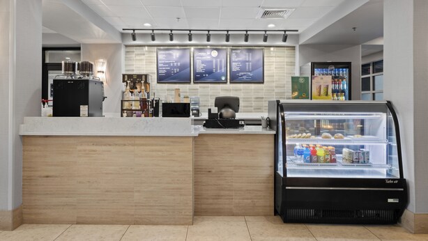 A modern coffee shop interior with a counter, espresso machines, a refrigerated display case, and menu boards.