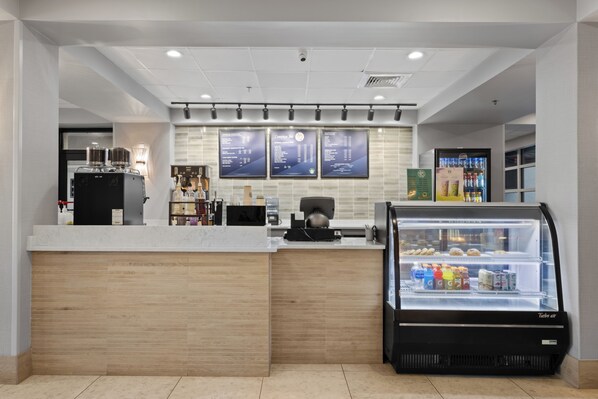 A modern coffee shop interior with a counter, espresso machines, a refrigerated display case, and menu boards.