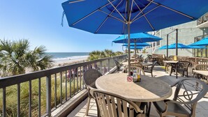 An outdoor seating area with blue umbrellas, a view of the beach, and a no-smoking sign.
