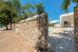 A stone wall with a door, a pool area with lounge chairs, and a covered seating area.