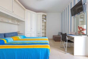 A bedroom with a bed, a desk, a chair, and a TV.