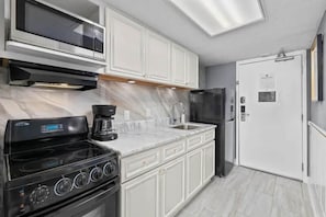Una cocina moderna con armarios blancos, una estufa negra, una cafetera y un microondas.