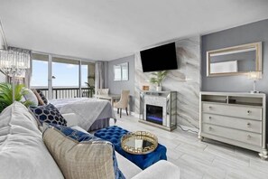 Una sala de estar moderna con sofá, un reposapiés azul, chimenea, televisor montado en la pared y un comedor.