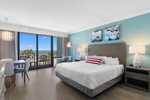 A hotel room with a large bed, a balcony with chairs, and artwork on the wall.