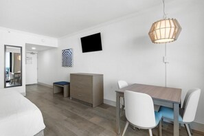 Ein modernes Hotelzimmer mit Bett, Schreibtisch mit Stühlen, Kommode, Fernseher und einer ungewöhnlichen sechseckigen Leuchte.