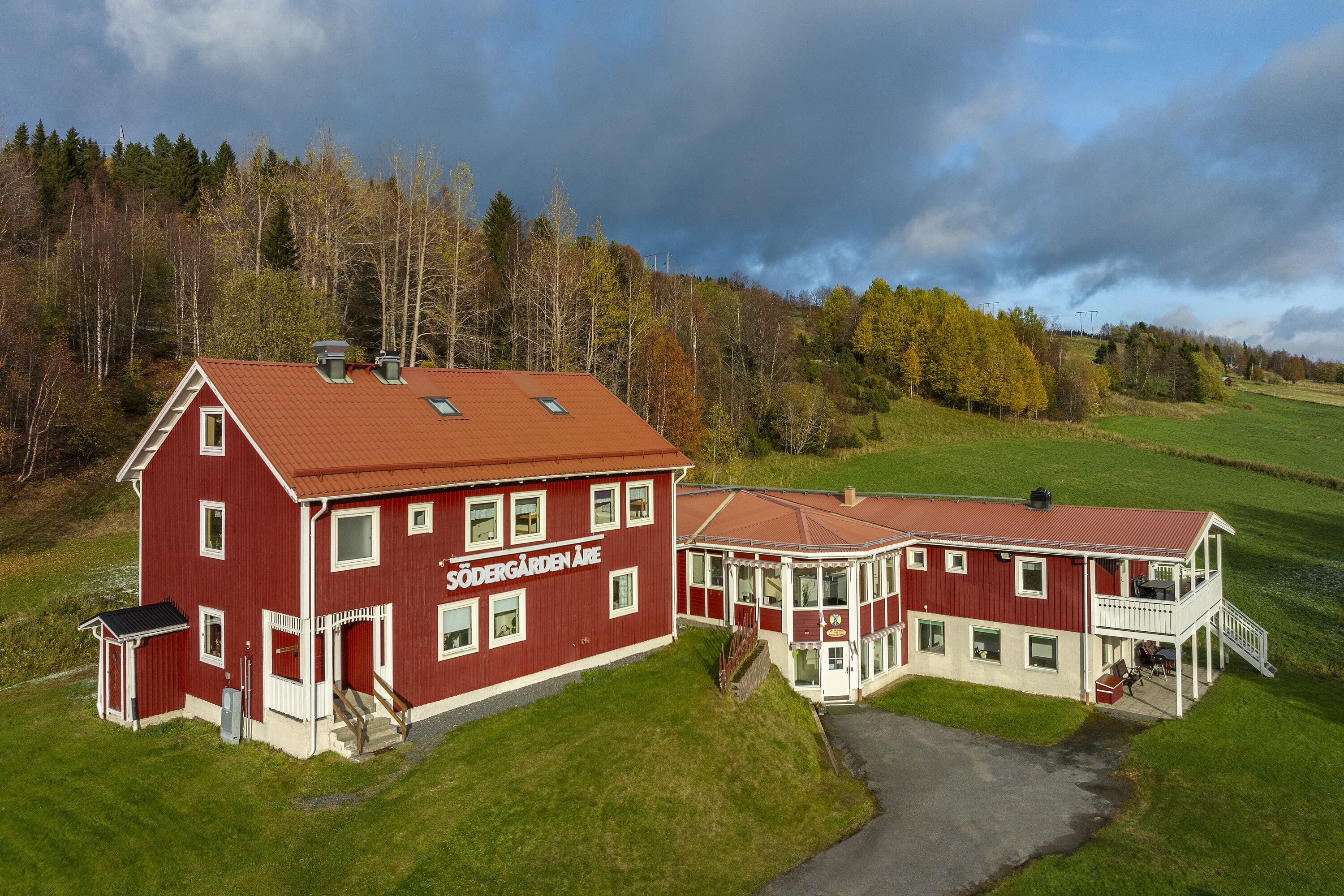 Un bâtiment rouge et blanc doté d’un grand porche et d’un balcon, entouré d’un paysage verdoyant et d’arbres.
