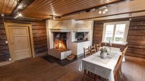 A log cabin interior with a central fireplace, wooden dining table, and chairs. - Södergården Åre (Undersaker)