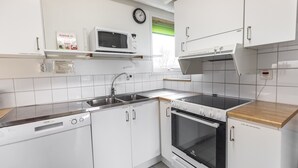 A modern kitchen with white cabinets, a microwave, a dishwasher, and an oven. - Södergården Åre (Undersaker)