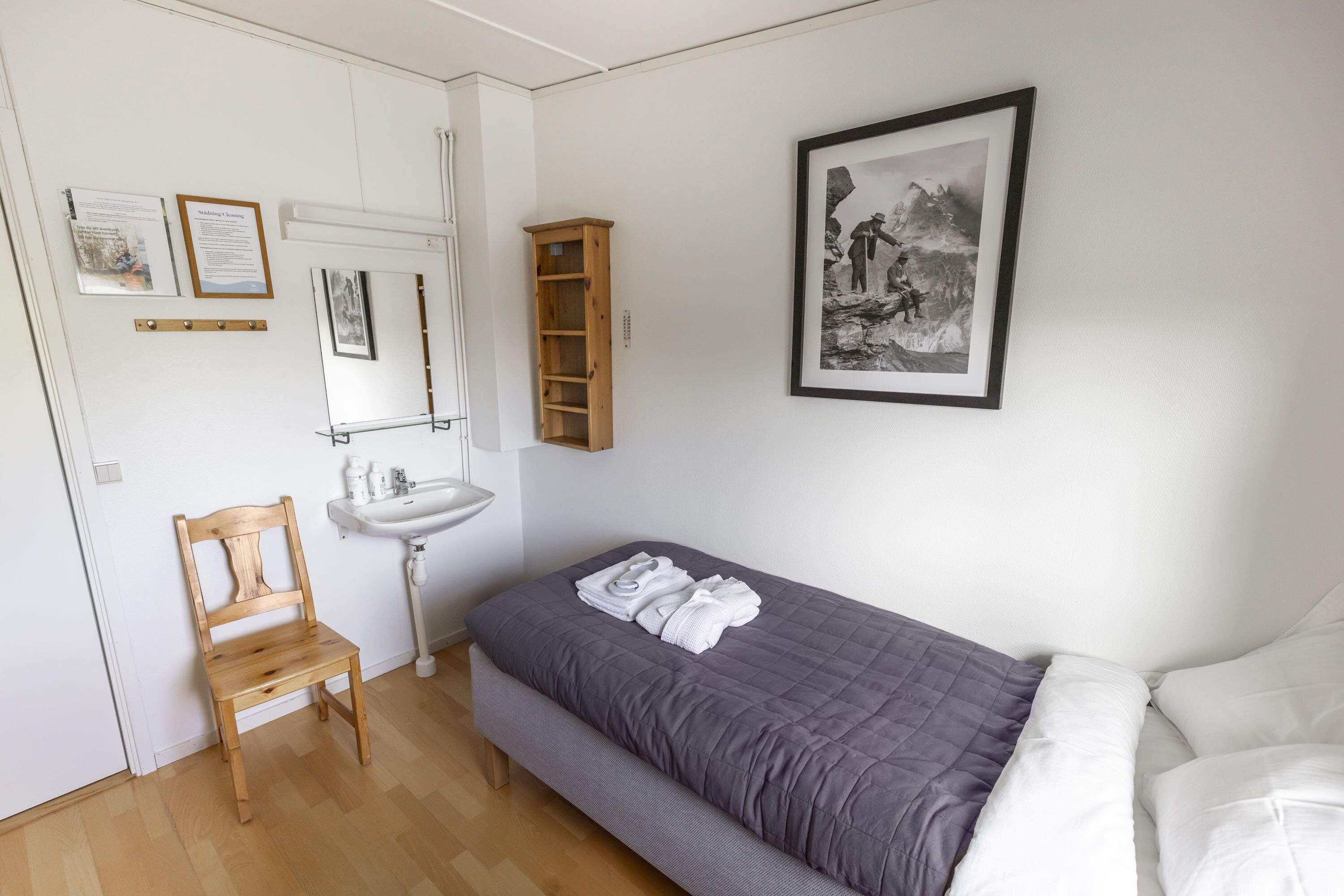 A bedroom with a bed, a wooden chair, a white sink, and a framed picture on the wall.