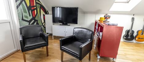 A room with a flat-screen TV, two black leather chairs, a red cabinet, and a guitar wall.