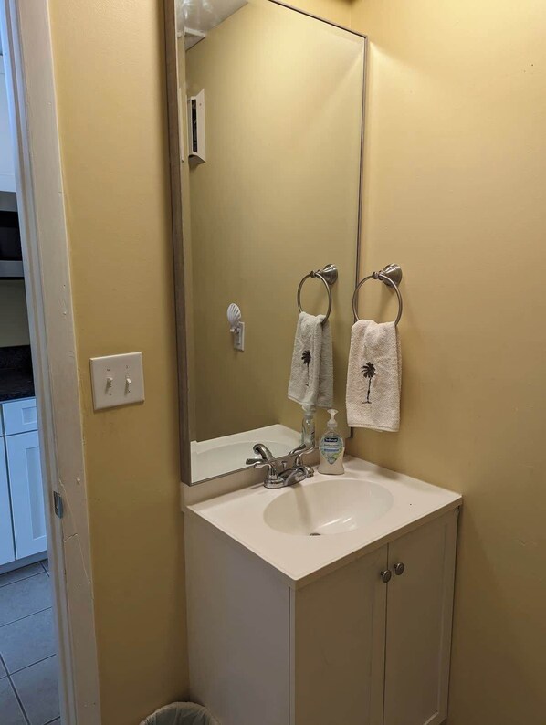 A bathroom with a white sink, a mirror, two towels, and a soap dispenser. - Ocean Therapy (Carolina Beach)