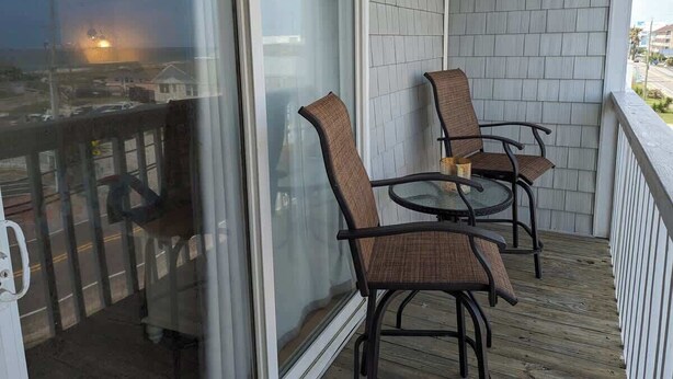A balcony with two wicker chairs and a glass table, overlooking a residential area. - Ocean Therapy (Carolina Beach)