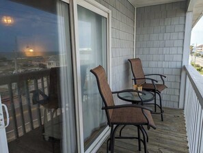 A balcony with two wicker chairs and a glass table, overlooking a residential area. - Ocean Therapy (Carolina Beach)