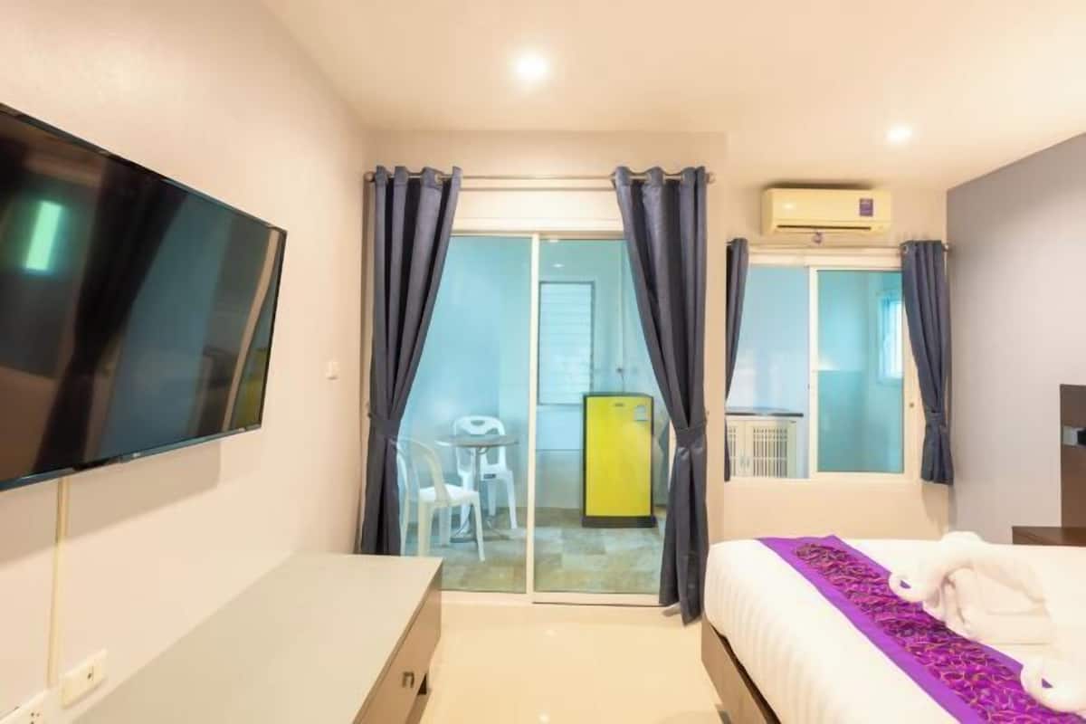 A hotel room with a bed, a flat-screen TV, a sliding glass door leading to a balcony, and a yellow minibar.