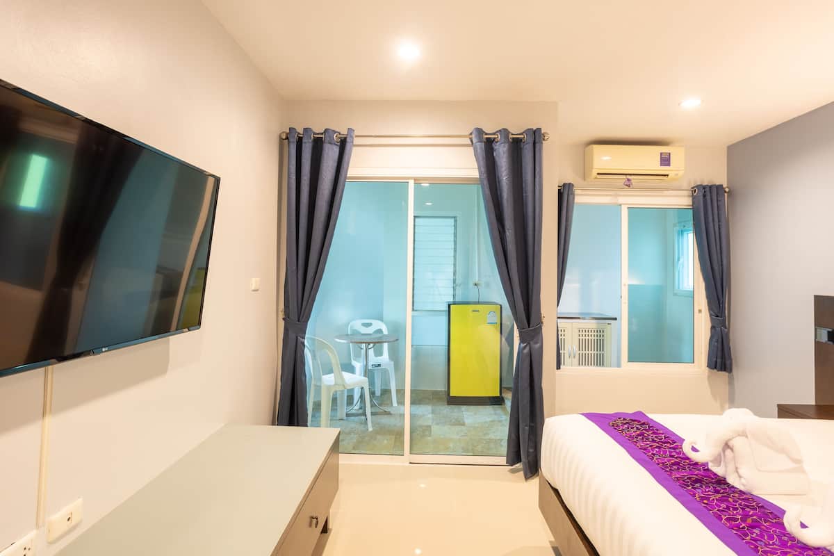 A hotel room with a bed, a TV, a desk, and a sliding door leading to a balcony.