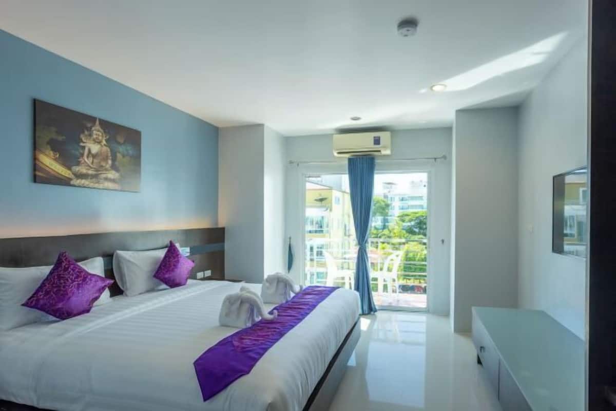 A modern hotel room with a bed, a painting, a window with a view, and a ceiling fan.