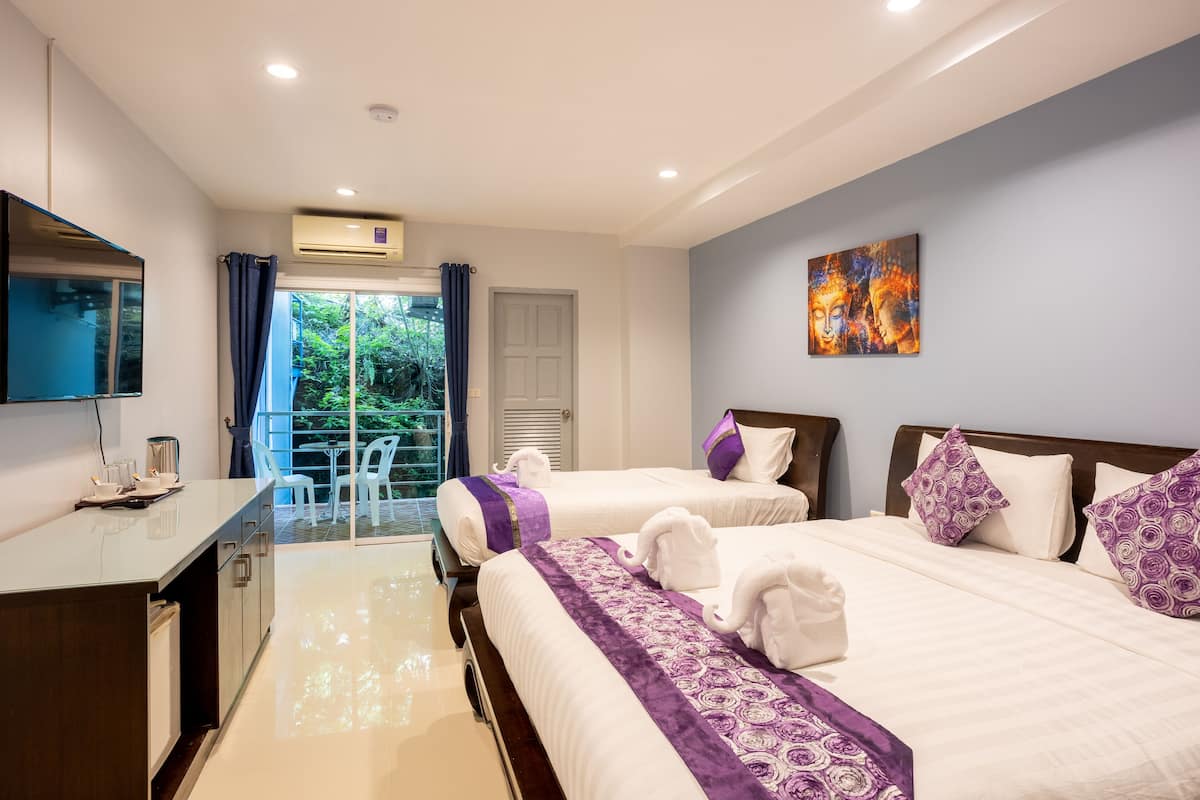 A hotel room with two beds, a desk, a TV, and a balcony with a view of greenery.