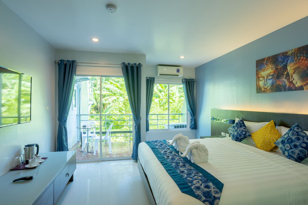 A hotel room with a bed, a desk, a chair, and a view of greenery outside.