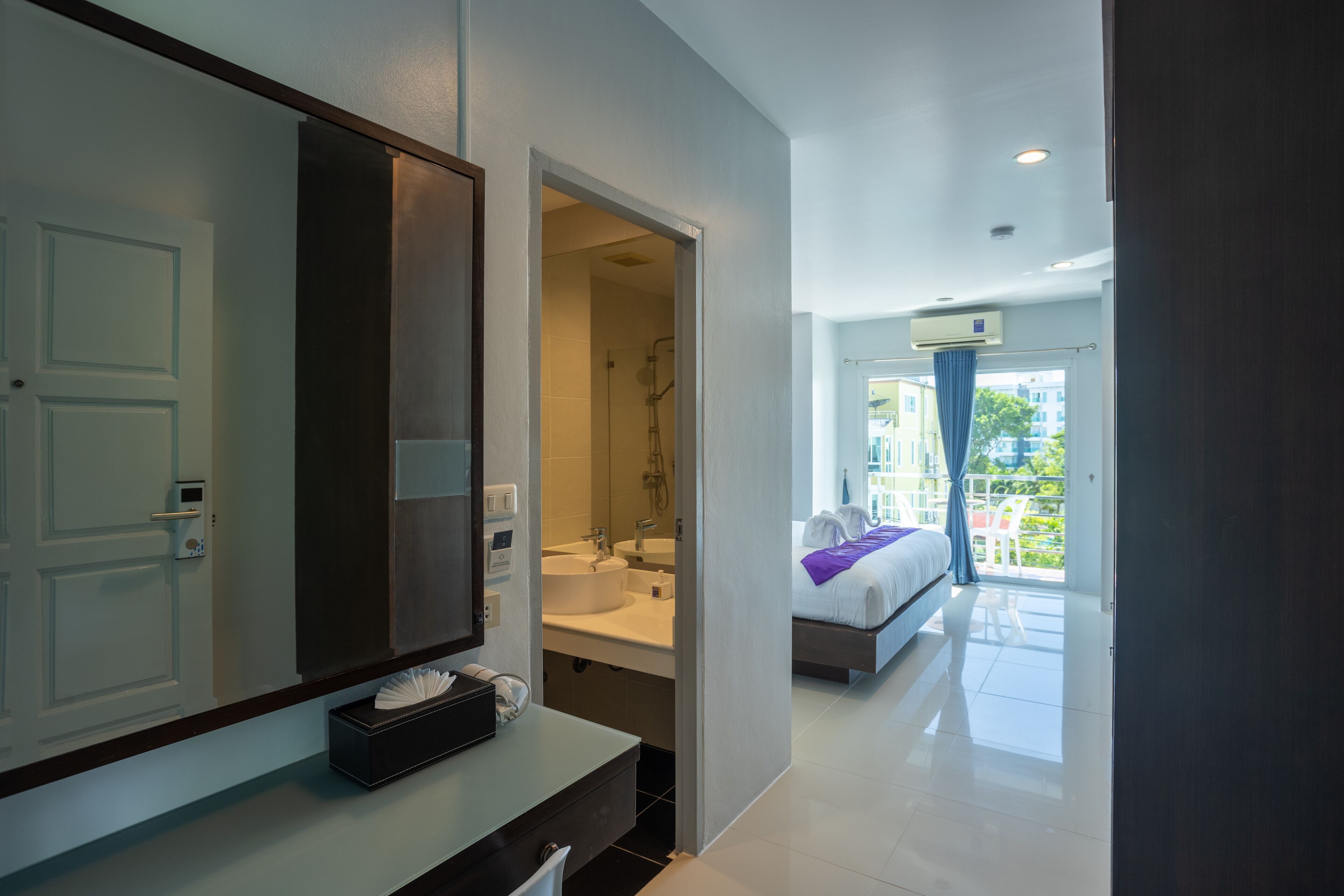 A modern hotel room with a large mirror, a vanity with a sink, a bed with a view of the outdoors, and a balcony.