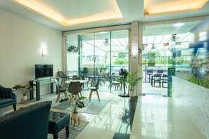 A modern living room with a sofa, TV, and a glass door leading to an outdoor dining area. - The Great at Patong Hotel (Patong)