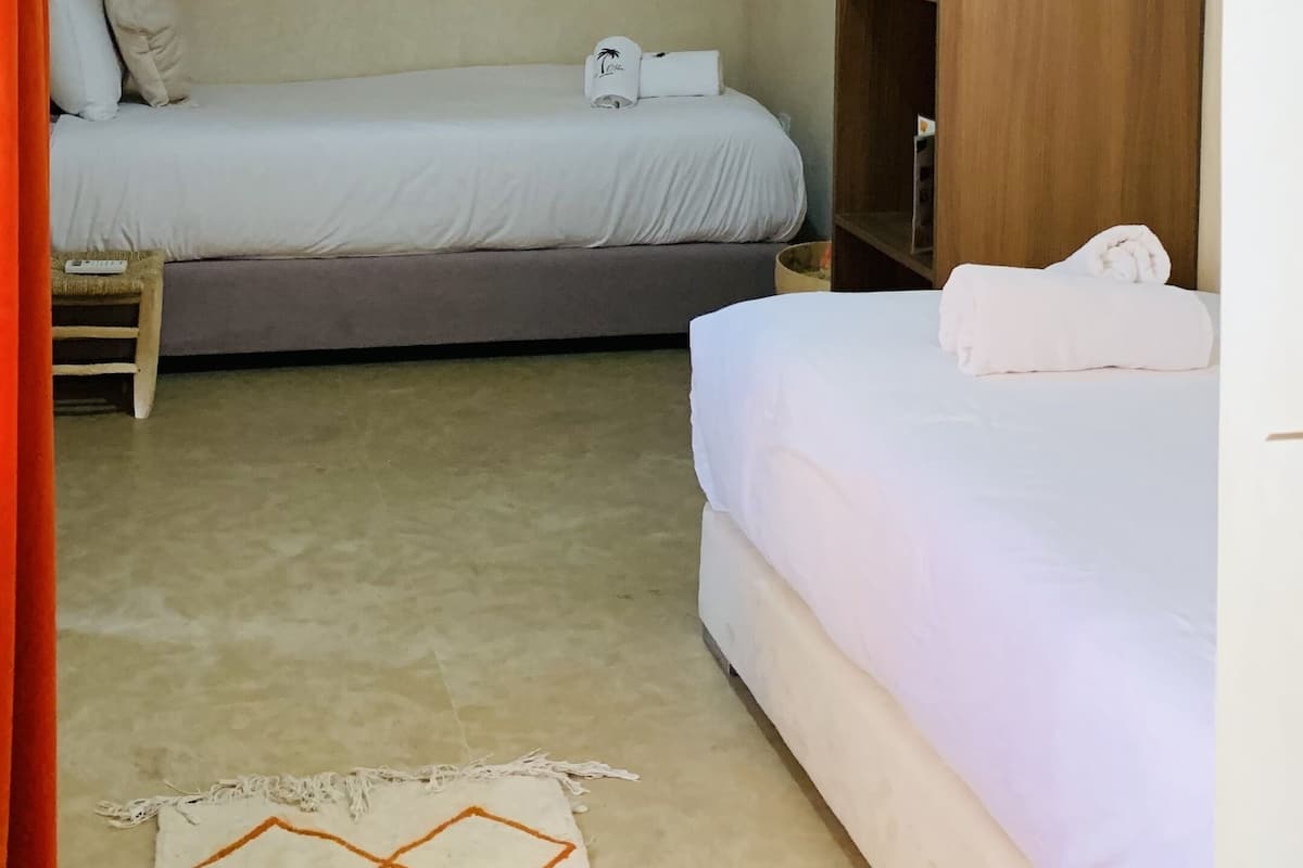A room with two beds, a wooden wardrobe, a hanging light fixture, and a patterned rug.