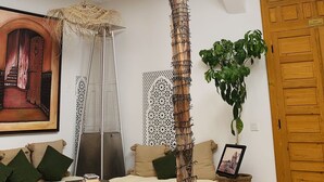 Una habitación con una palmera alta, un sofá, una silla colgante y una puerta de madera.
