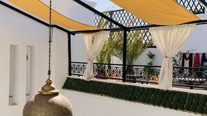Una terraza al aire libre de varios niveles con una lámpara colgante, toldos amarillos y plantas en macetas.