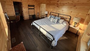 Un dormitori de cabana de fusta amb un llit, làmpades de nit, escriptori i una cadira penjant.