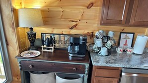 Cuina compacta amb armaris de fusta, una cafetera, tasses i un petit rentapeus.