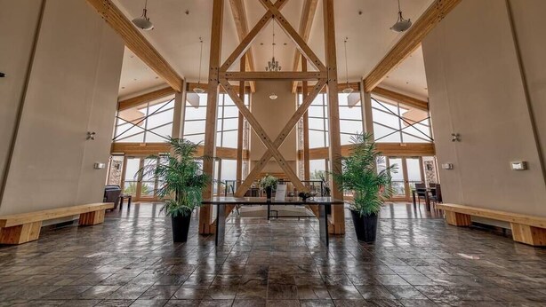 A spacious lobby with a high ceiling and wooden beams, large windows, and potted plants.