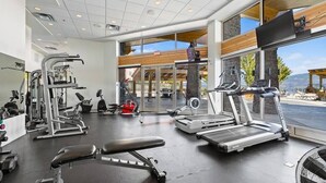 A gym with various exercise equipment, large windows, and a view of the outdoors.
