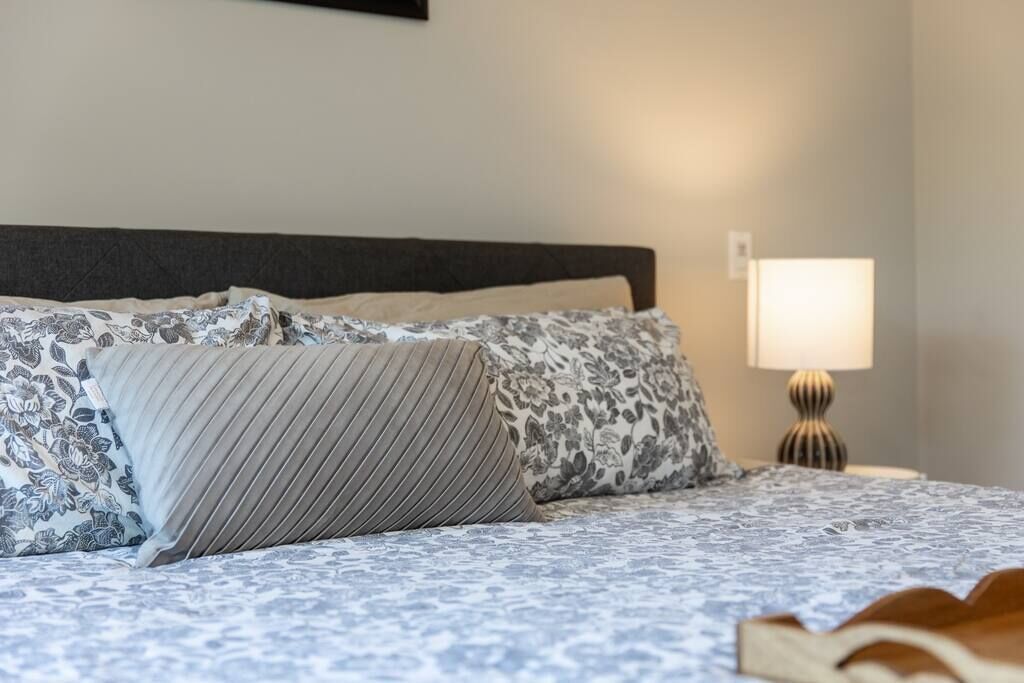 Un lit bien fait, avec une literie à motifs et des oreillers, une lampe de chevet et un livre posé sur le lit.